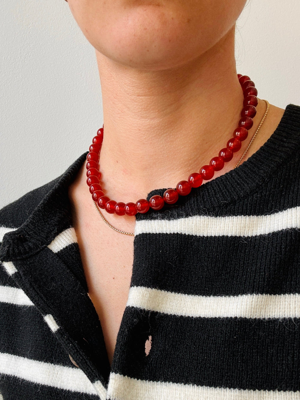 Person wearing a red beaded necklace with a black and white striped sweater.