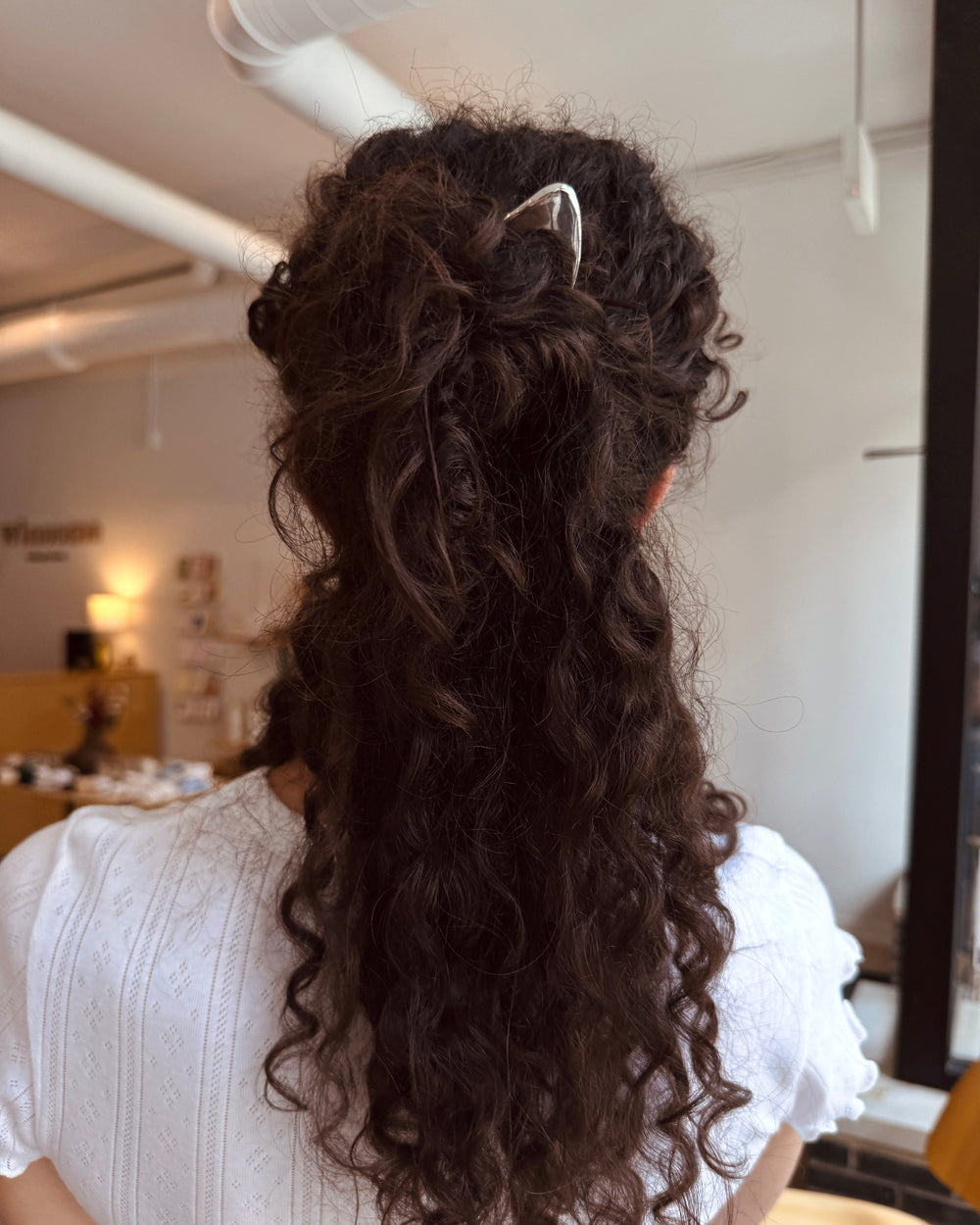 Person with long, wavy hair styled in an elegant updo with a silver hair pin, in an indoor setting.