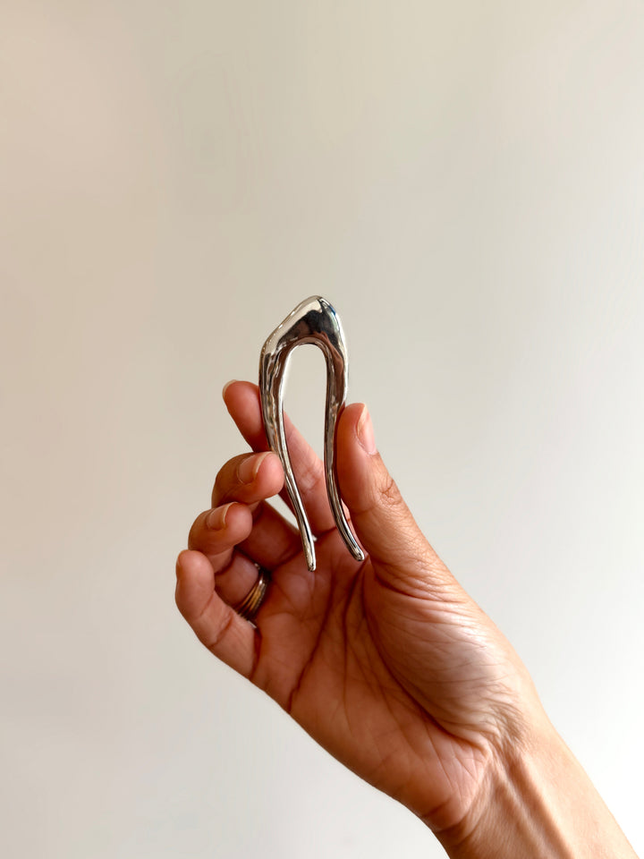 Hand holding a silver U-shaped hair pin against a plain background